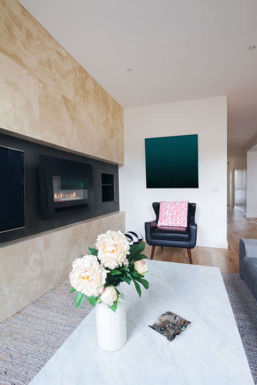 Modern living room with marble fireplace, black armchair, and white flowers on a marble table; accent wall with abstract art
