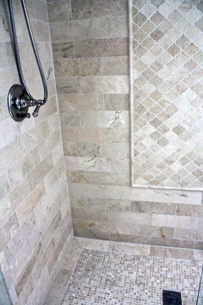 Beige marble shower with intricate patterned tile accent and handheld showerhead.