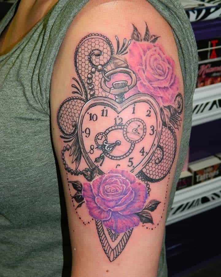 Upper arm tattoo featuring a heart-shaped pocket watch with Roman numerals, intricate lace patterns, and vibrant purple roses with beaded details.