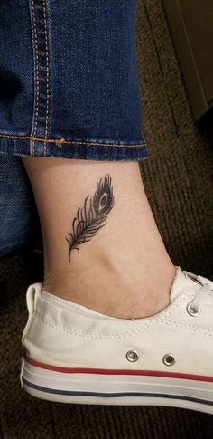 Small black ink peacock feather tattoo on the ankle, featuring fine linework and subtle shading for a minimalist and elegant look.