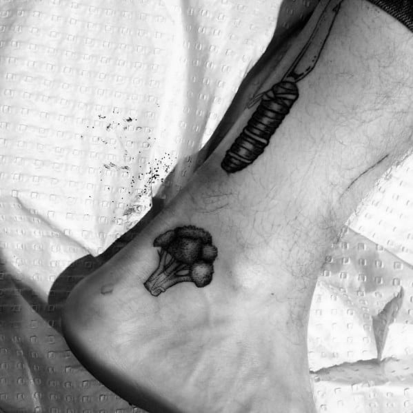 Small black ink broccoli tattoo on the ankle, featuring fine shading and bold details for a minimalist yet striking design.