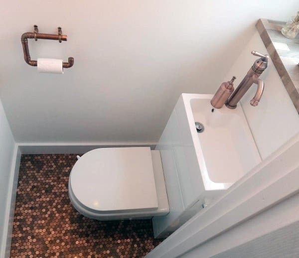 Compact bathroom with penny tile floor, space-saving toilet, and mini sink with copper faucet.