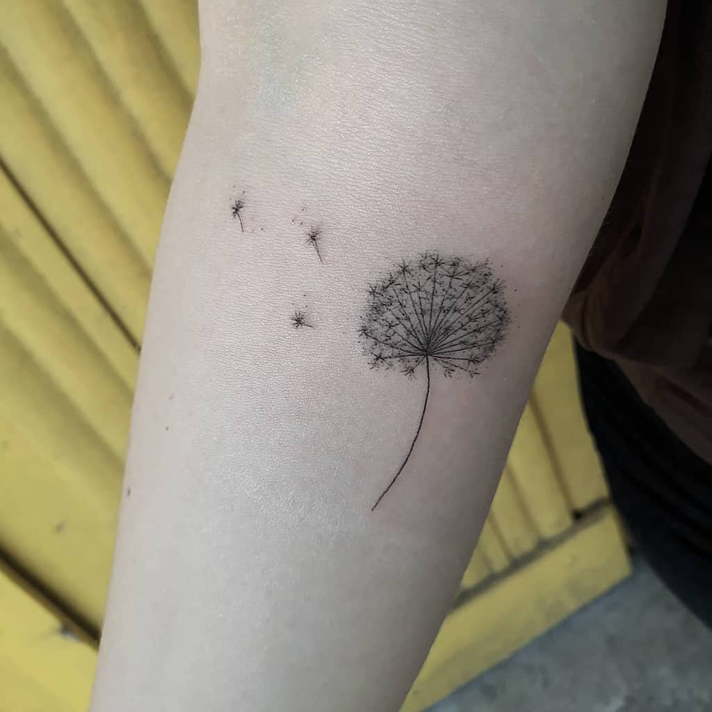 Fine-line dandelion tattoo on the forearm with seeds drifting away, symbolizing wishes, freedom, and new beginnings.