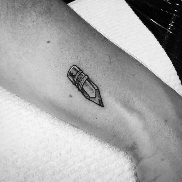A black and gray tattoo of a small pencil elegantly graces the arm, capturing simplicity with its fine details