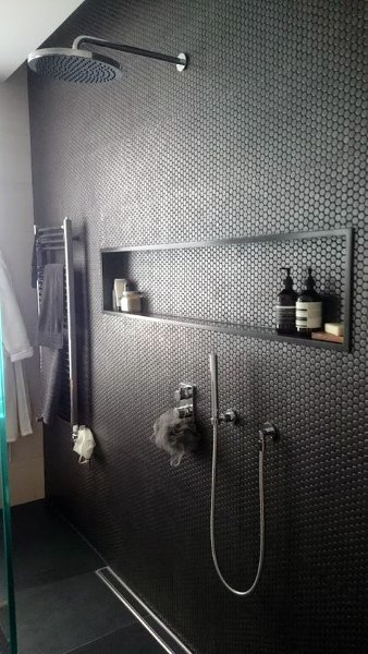 Black hexagonal tile shower with built-in shelf, rainfall showerhead, and sleek fixtures.