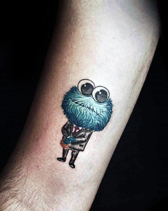Tiny Cookie Monster tattoo wearing a formal suit and red tie, holding a cookie with oversized eyes and a charming stance.