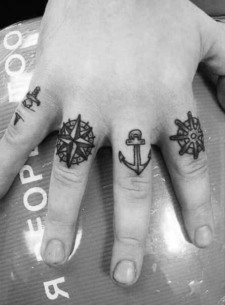 Black anchor, compass, and ship wheel tattoos on fingers of a hand