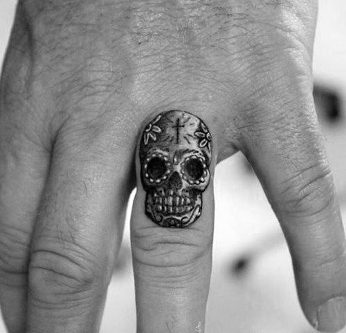 Close-up of a hand with a small skull tattoo on the middle finger
