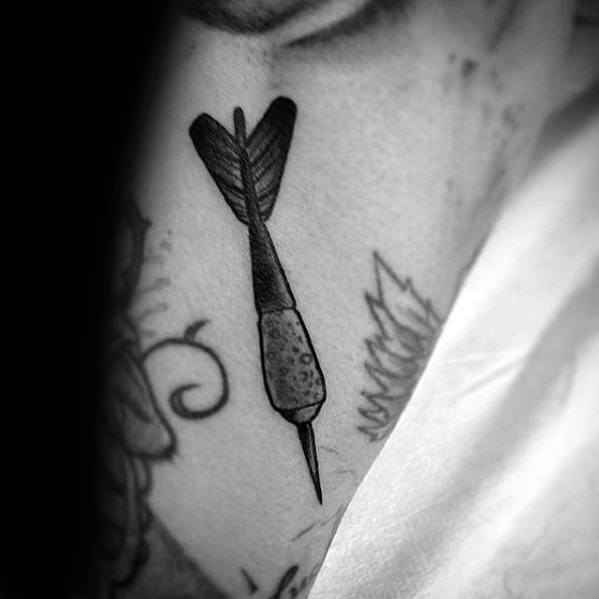 Small, simple black dart tattoo with fine shading, placed among other designs, symbolizing focus and direction in a minimalist style.