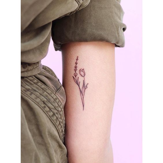 A delicate fine-line tulip tattoo on the upper arm, featuring a small tulip with botanical elements for a minimalist and elegant design.