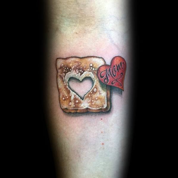 Realistic toast tattoo with a heart-shaped cutout, sprinkled with sesame seeds, and a red heart tag reading "Mom," blending warmth with nostalgia.