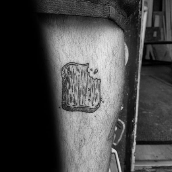 Minimalist black ink toast tattoo with a bite taken out, featuring fine lines and subtle shading for a simple yet artistic design on the leg.