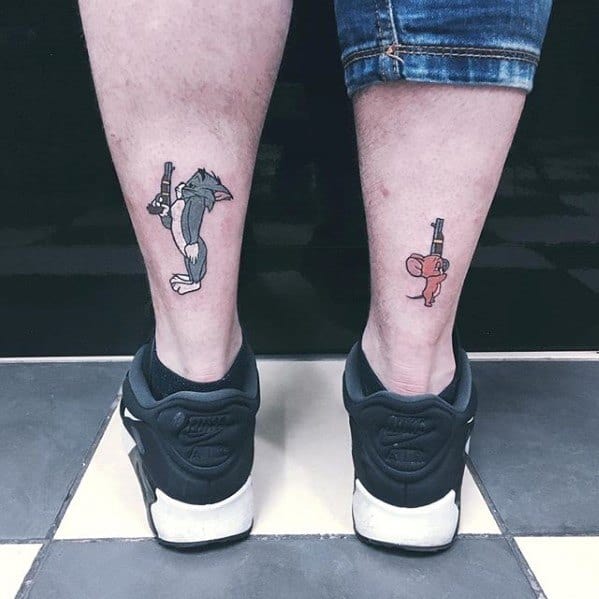 Matching tattoos on the backs of both legs showing Tom with a gun on one side and Jerry with a gun on the other in cartoon style.