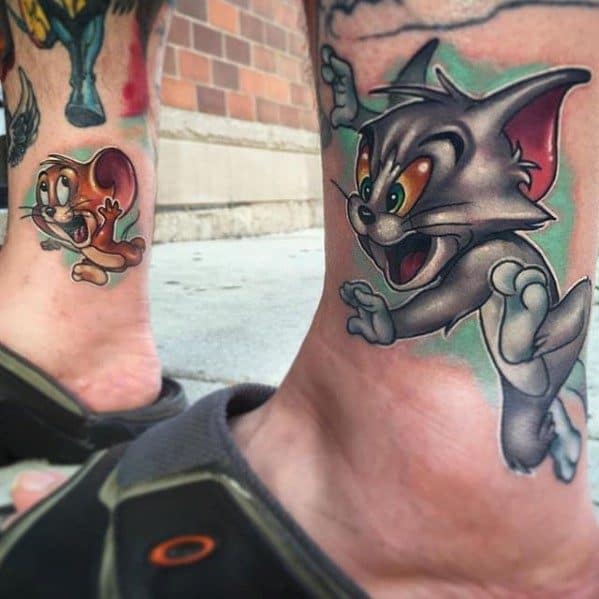 Colorful ankle tattoos of Tom leaping after Jerry, inked on separate legs with vibrant shading and classic cartoon expressions.
