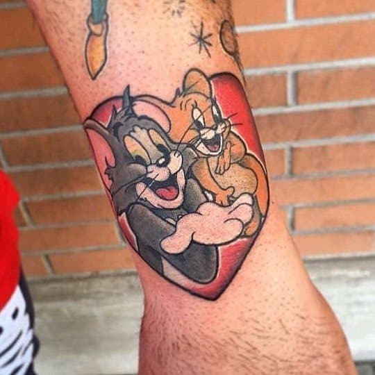 Colorful tattoo of Tom and Jerry hugging inside a red heart, symbolizing friendship and love in playful cartoon style.