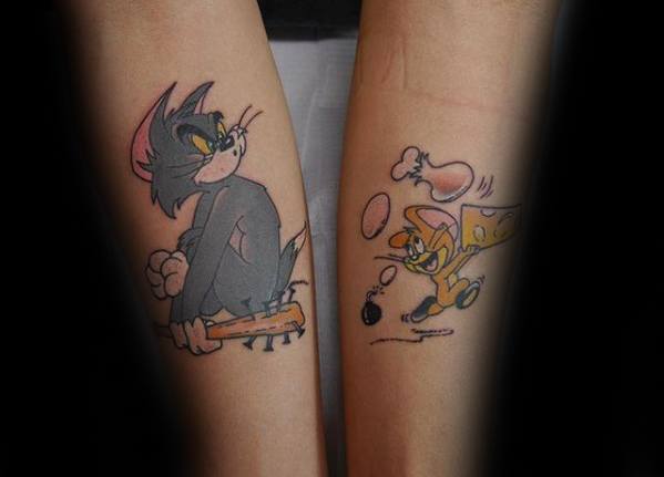 Matching forearm tattoos of Tom holding a bat and Jerry running with cheese, bombs, and food flying around in cartoon chaos.
