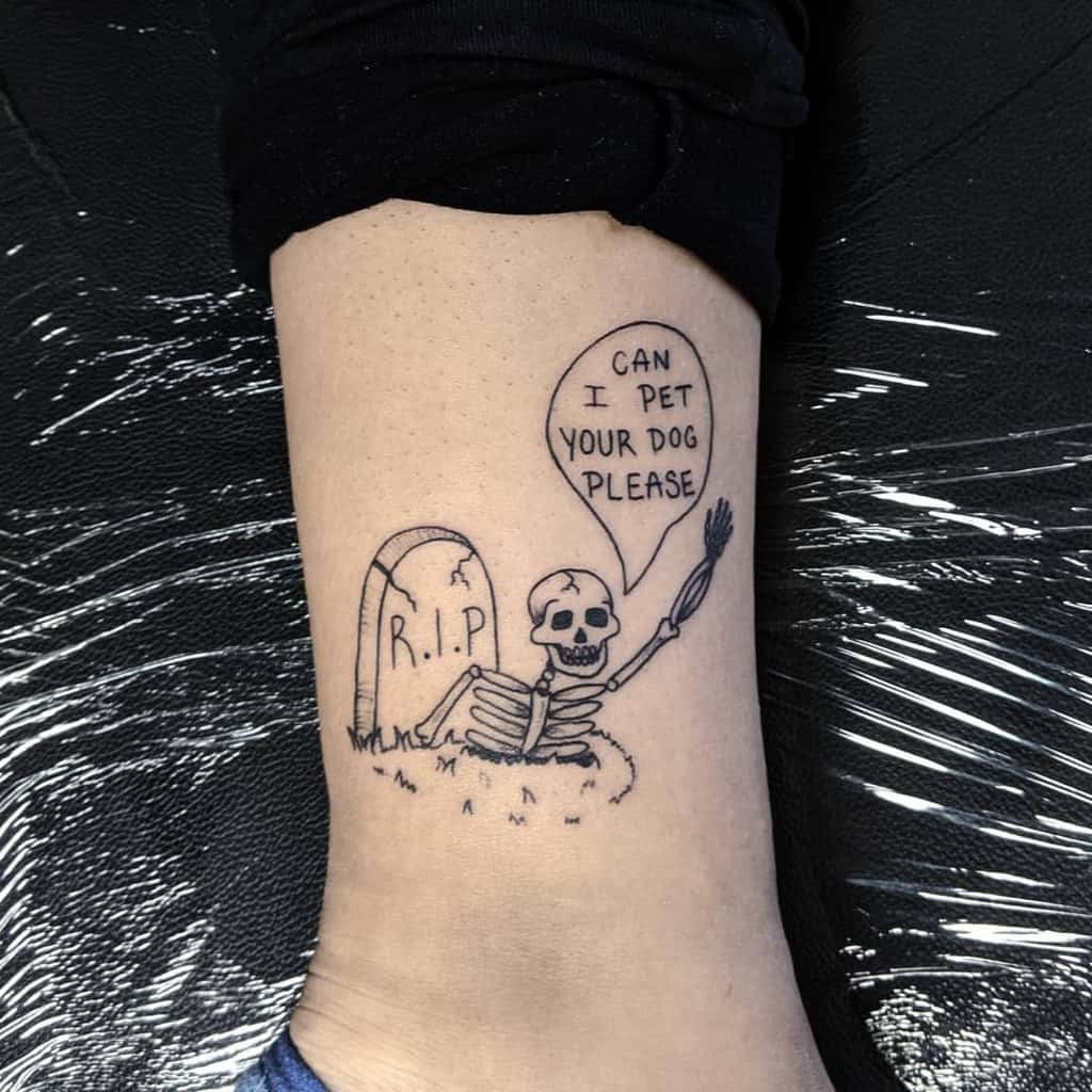 A black ink tattoo of a skeleton rising from a grave marked 'R.I.P.,' with a speech bubble saying 'Can I pet your dog please,' adding a humorous twist.