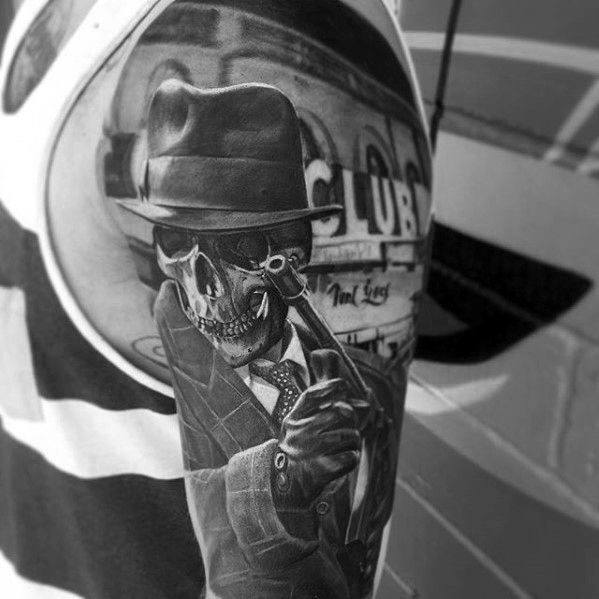 Realistic black and grey gangster tattoo featuring a skeleton in a fedora and suit holding a Tommy gun, with the Cotton Club in the background for a vintage crime theme.