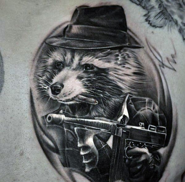 Black and grey tattoo of a raccoon dressed as a gangster, wearing a fedora and suit, holding a Tommy gun, with detailed shading for a unique mobster look.