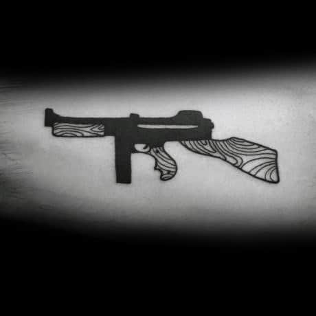 Minimalist Tommy gun tattoo with bold black shading and wood grain detailing, creating a clean and stylish firearm design on the forearm.