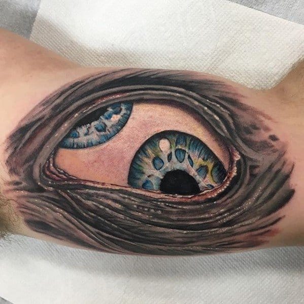 Realistic Tool-inspired tattoo of two vivid blue-green eyes peeking through torn skin with detailed texture and 3D shading on the arm.