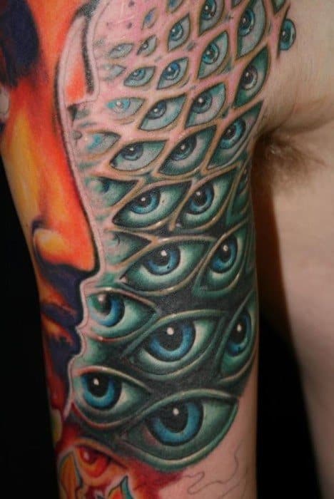 Colorful Tool-inspired upper arm tattoo featuring a profile silhouette and a cascade of layered blue eyes in a psychedelic, surreal pattern.