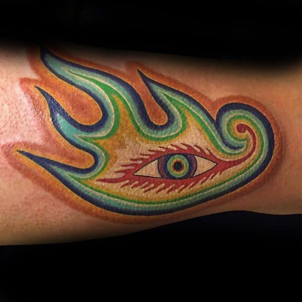 Vibrant Tool-inspired tattoo of a flaming eye in rainbow tones, with sharp edges and a psychedelic design wrapping around the forearm.