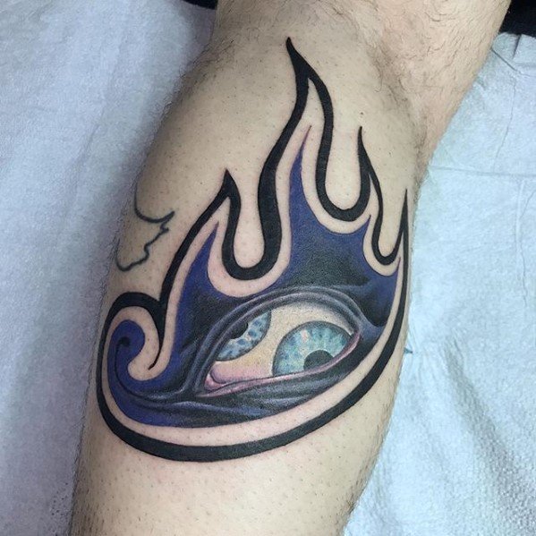Tool-inspired leg tattoo of a blue flame design encircling a realistic eye with vibrant blue and green tones, blending surreal and bold styles.