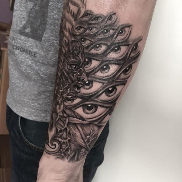 Black and grey Tool-inspired forearm tattoo featuring a cluster of layered eyes merging with an abstract face and intricate textures.