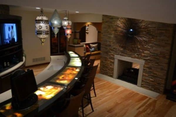 Stylish basement lounge with a curved bar, hanging lanterns, and a stone fireplace