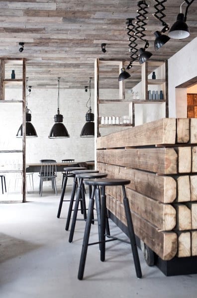 Minimalist cafe interior with wood accents, a sleek bar, black bar stools, and hanging black pendant lights