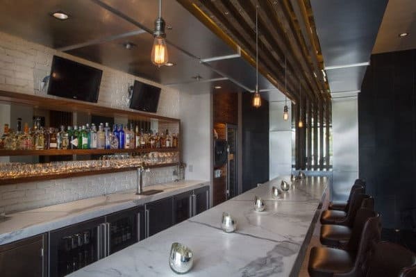 Modern bar interior with marble countertop, bar stools, bar shelves of bottles, and pendant lighting