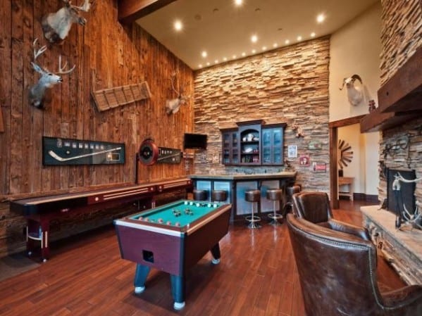 Rustic game room with pool table, shuffleboard, leather chairs, wood walls, and mounted animal heads