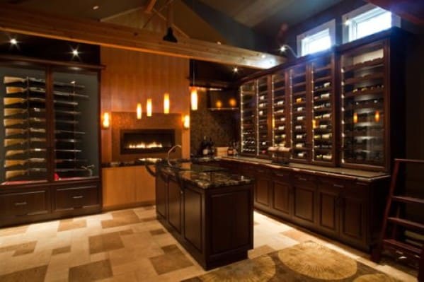 A dimly lit wine cellar with wooden cabinets, a marble island, and a wall-mounted fireplace