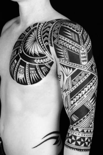 Person with intricate black geometric tattoos on chest, shoulder, and arm