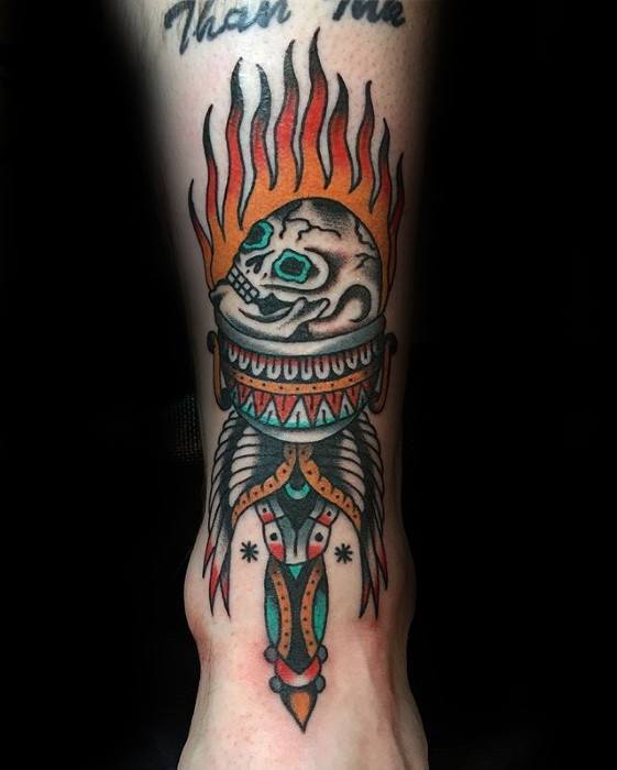 Colorful torch tattoo with a flaming skull at the top, turquoise eye sockets, and a handle adorned with tribal-inspired patterns and feathers.