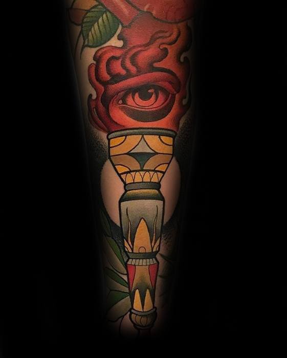 Vibrant torch tattoo with a red flame forming an eye, bold geometric handle, and subtle floral accents near the base.