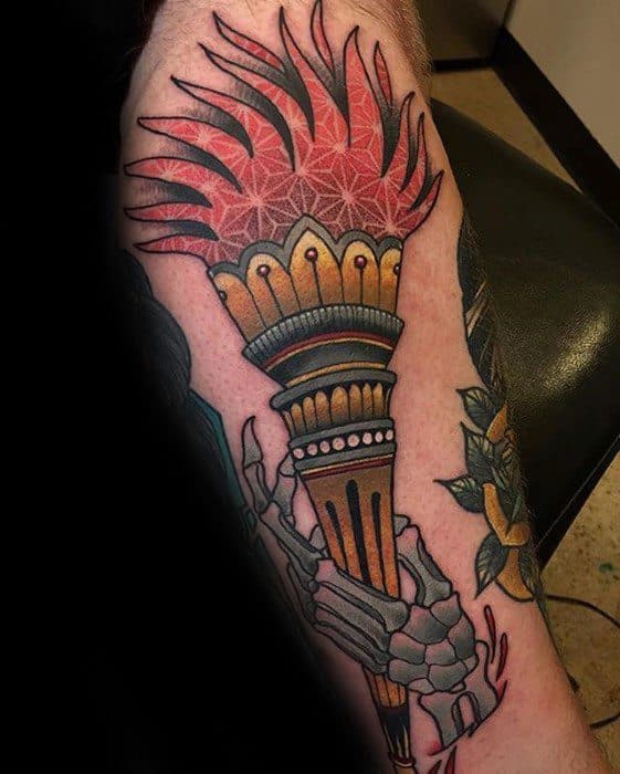 Torch tattoo with red patterned flames, a gold and teal ornamental top, and a skeletal hand gripping the base of the handle.
