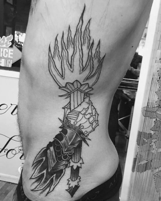 Linework torch tattoo on the side of the torso featuring a medieval armored hand gripping the torch, with tall, stylized flames above.