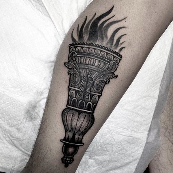 Ornate black and grey torch tattoo with detailed baroque-style carvings on the handle and softly shaded flames above.