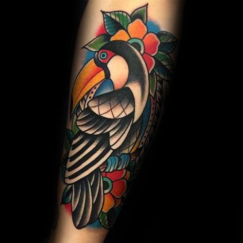 Neo-traditional toucan tattoo on the forearm with bold outlines, black and white feathers, and vibrant floral background elements.