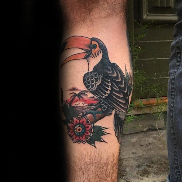 Traditional toucan tattoo on the leg with bold black shading, a red-orange beak, tropical flower, and sunset background elements.