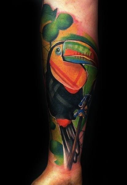 Vibrant toucan tattoo on the forearm with a large orange and green beak, set against abstract leaves and bold color gradients.
