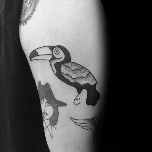 Simple blackwork toucan tattoo on the upper arm with clean lines and stippled shading for a bold, minimalist look.