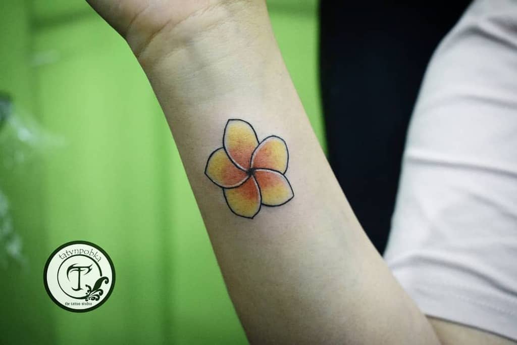 Colorful plumeria flower tattoo on a person's forearm