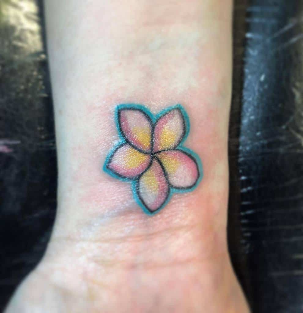 A colorful plumeria flower tattoo on a person's wrist