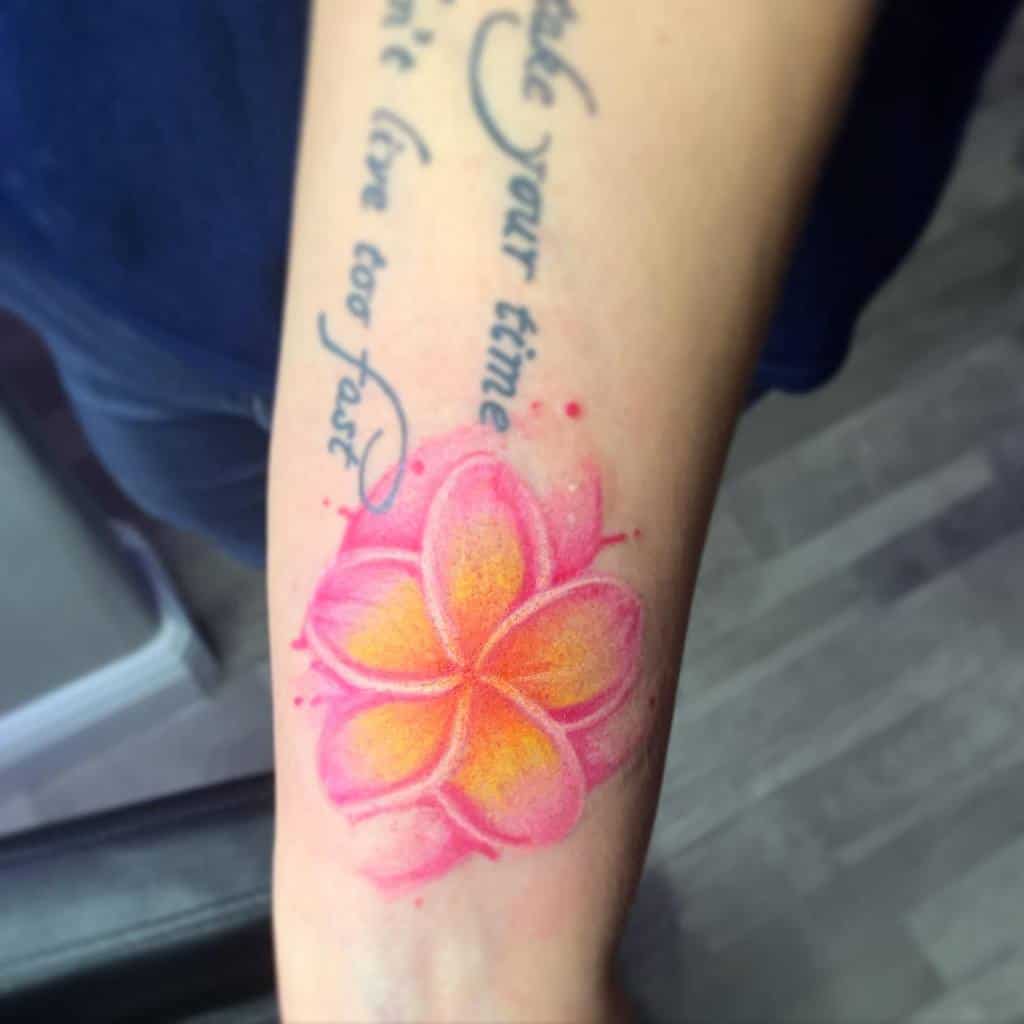 Colorful plumeria lflower tattoo with script text on a forearm