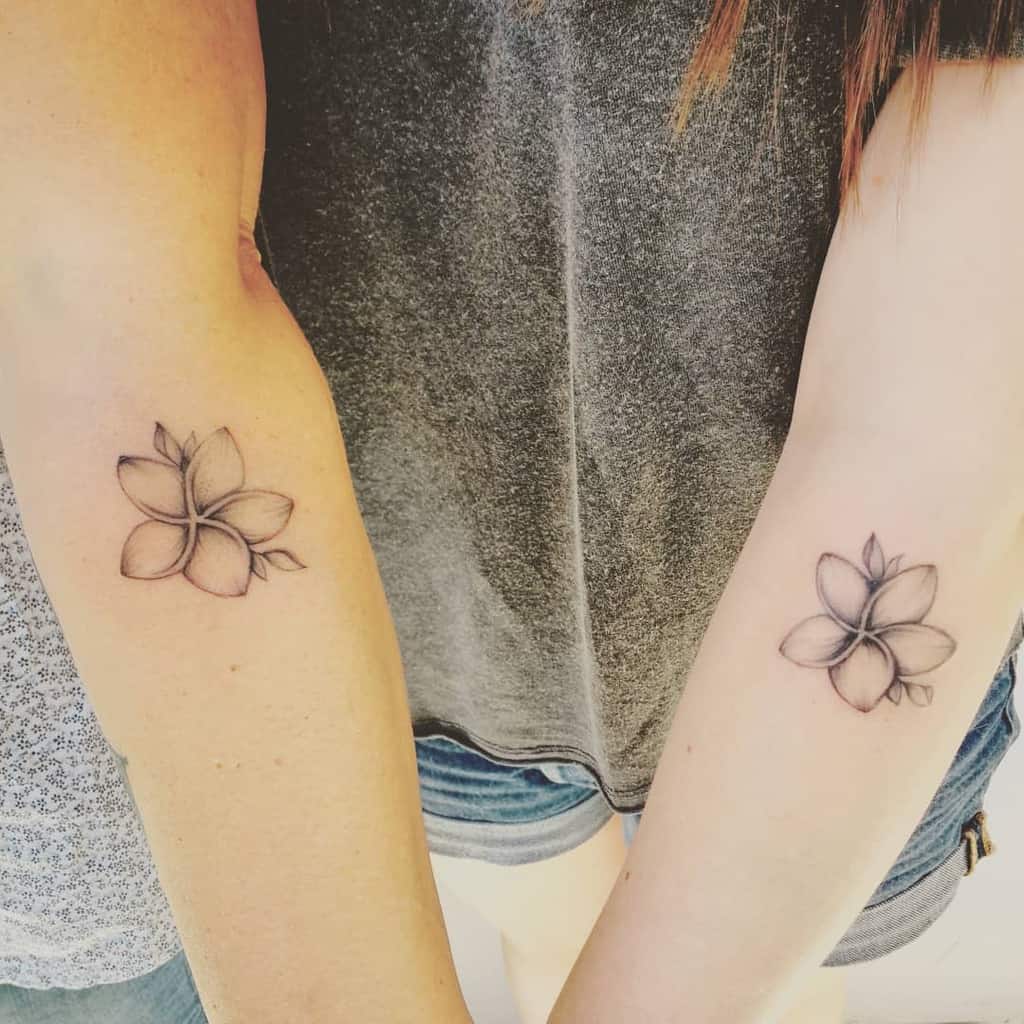 Two arms with matching plumeria flower tattoos, one on each forearm