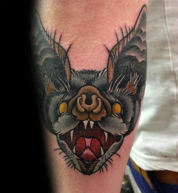 Traditional bat head tattoo with fierce yellow eyes, sharp fangs, and dark shading, featuring detailed ears and bold outlines.