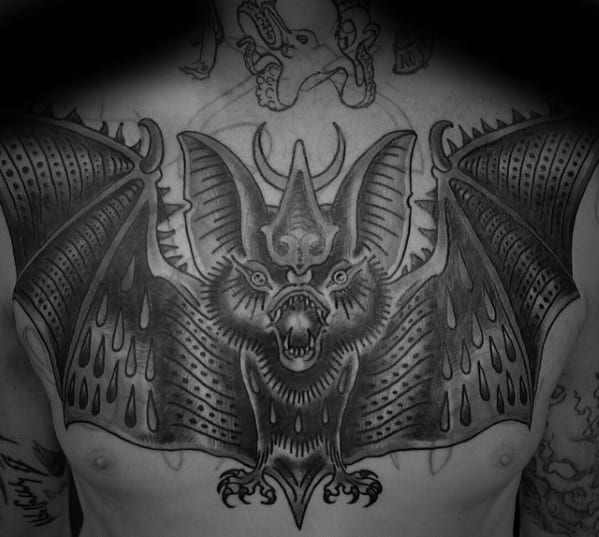 Large black and grey bat tattoo across the chest with outstretched wings, intricate shading, and fierce expression.